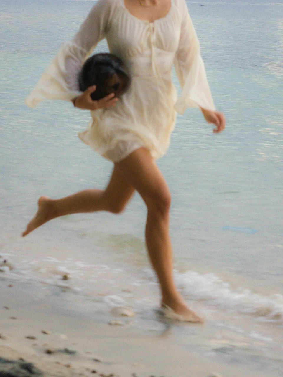 Woman in a white dress running on a beach with a coconut