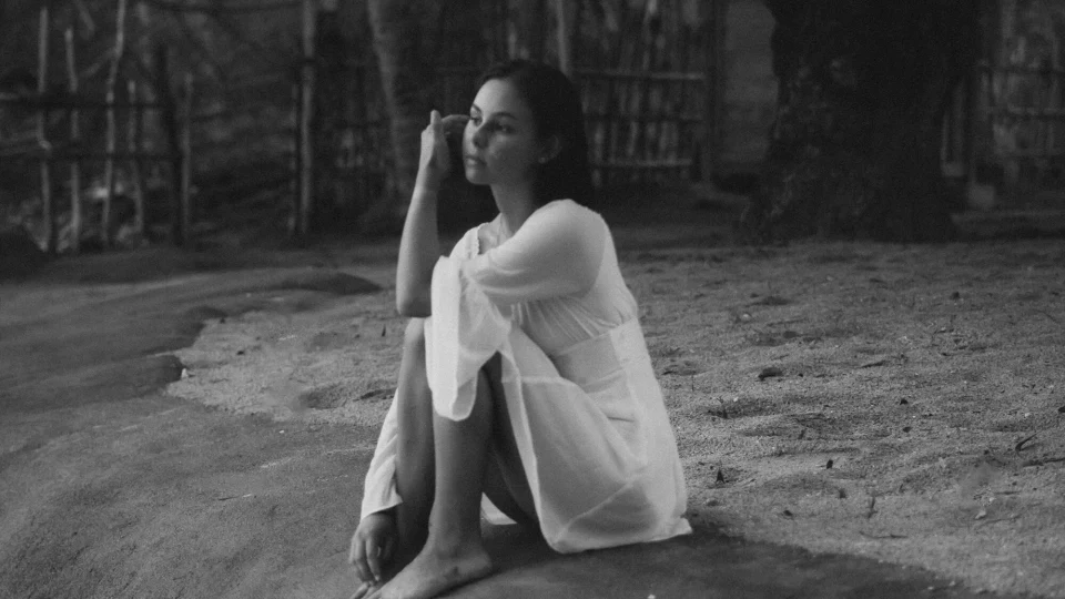 Woman in a white dress brushing hair from her face while sitting on a rock