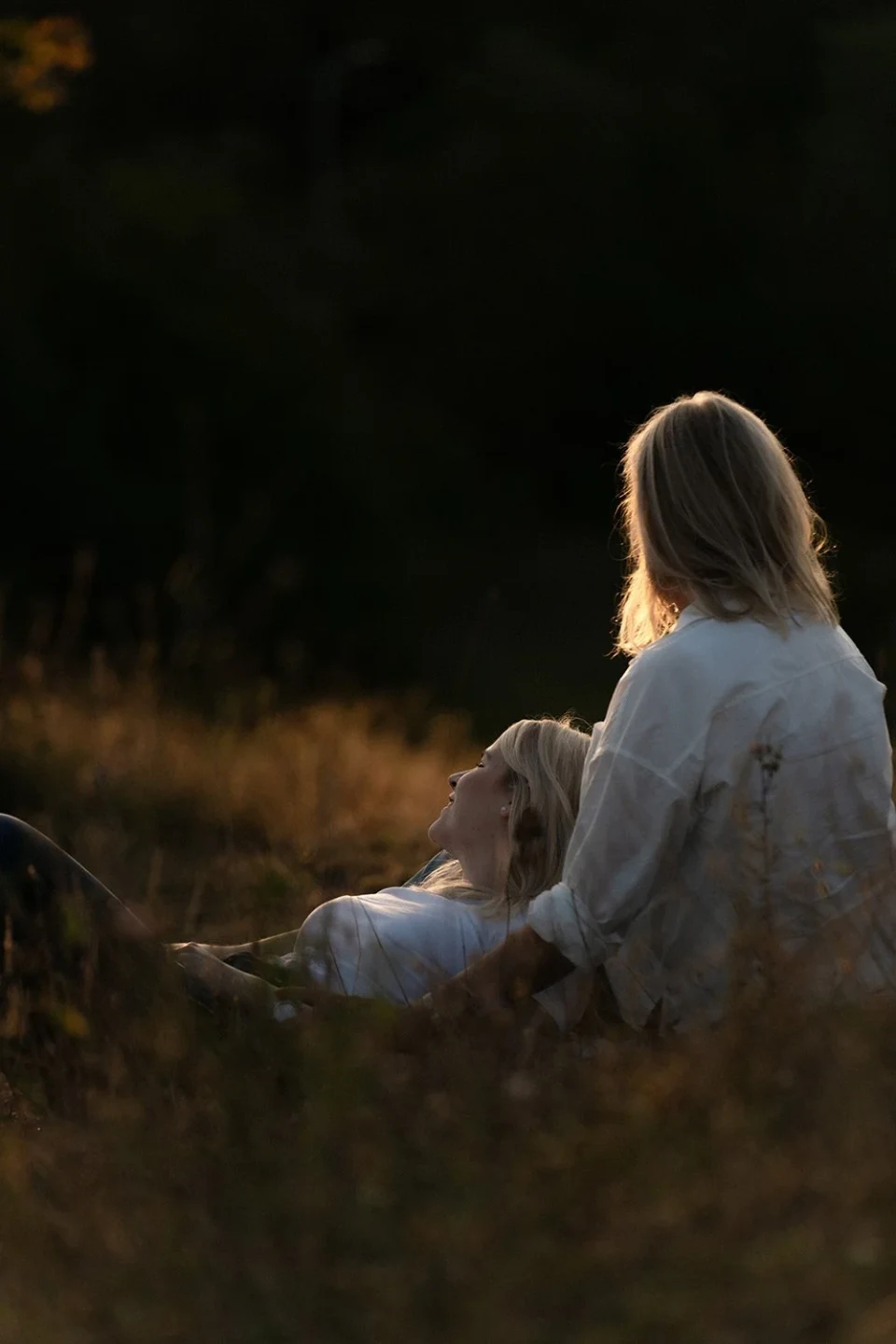 Daughter lying in her mother's lap in a meadow at sunset