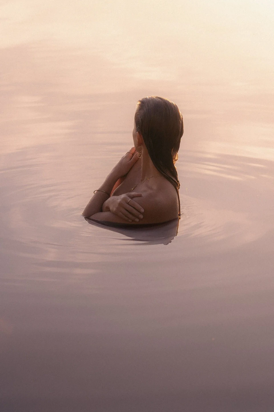 Woman in a lake at sunset, seen from behind