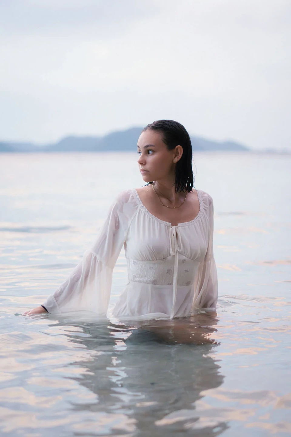Woman in a white dress sitting in water and looking to the side
