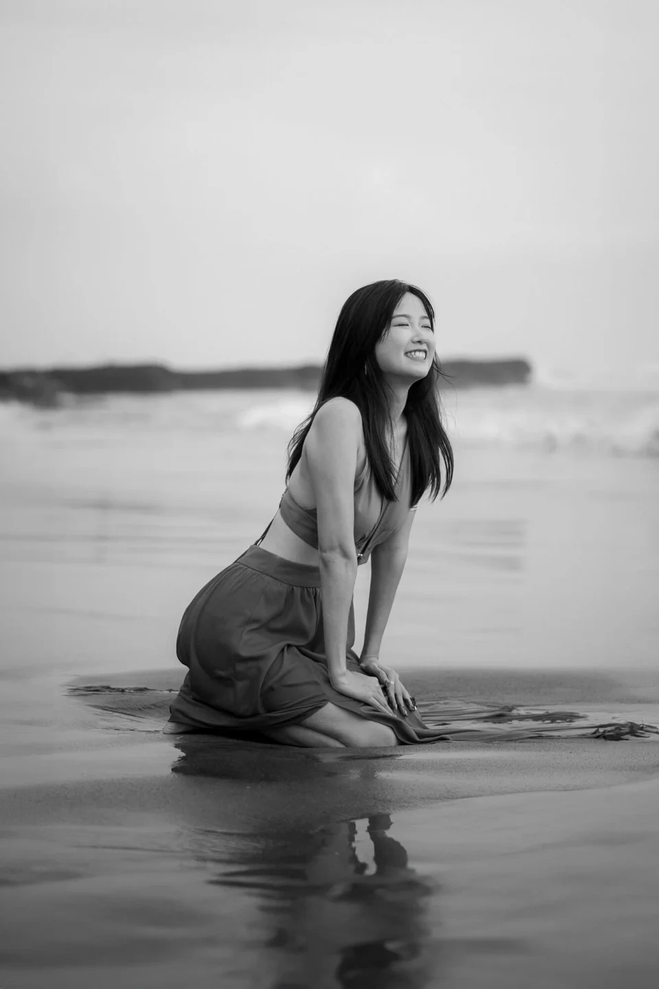 Woman kneeling on a beach and laughing