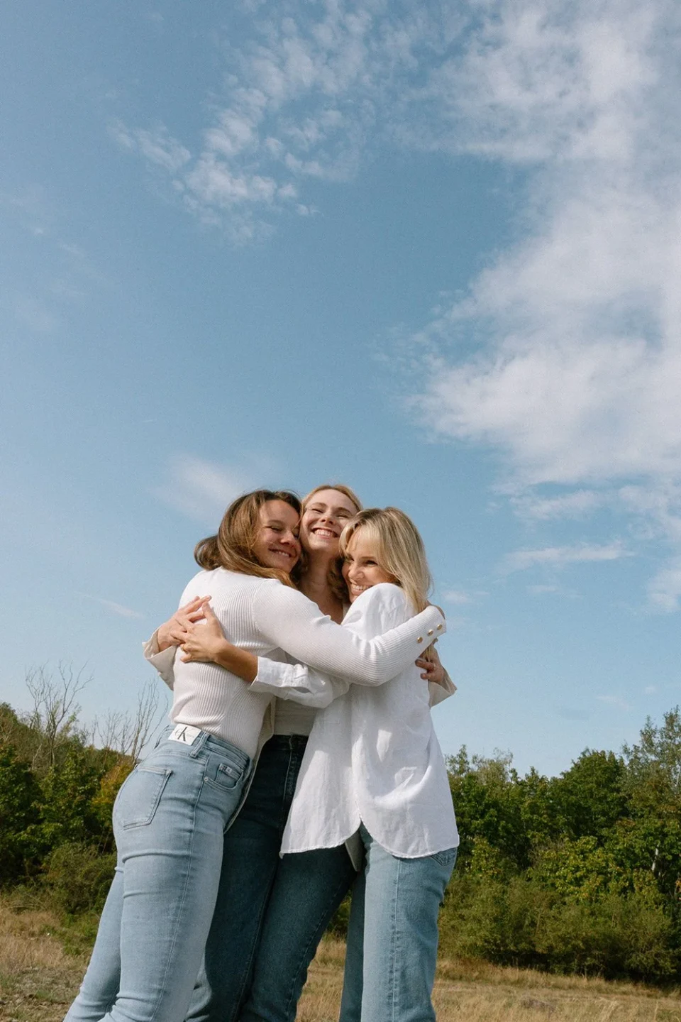 Three friends embracing against a blue sky